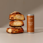 Stack of bread rolls next to a can of Protein Coffee on a neutral background