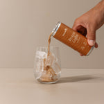 Hand pouring Protein Coffee from a can into a glass on a beige background
